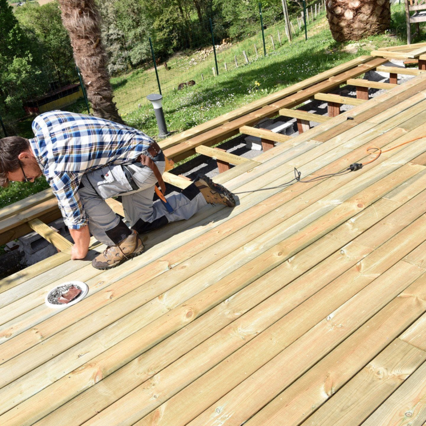 Carpenter kneeling on joists, screwing down new deck boards