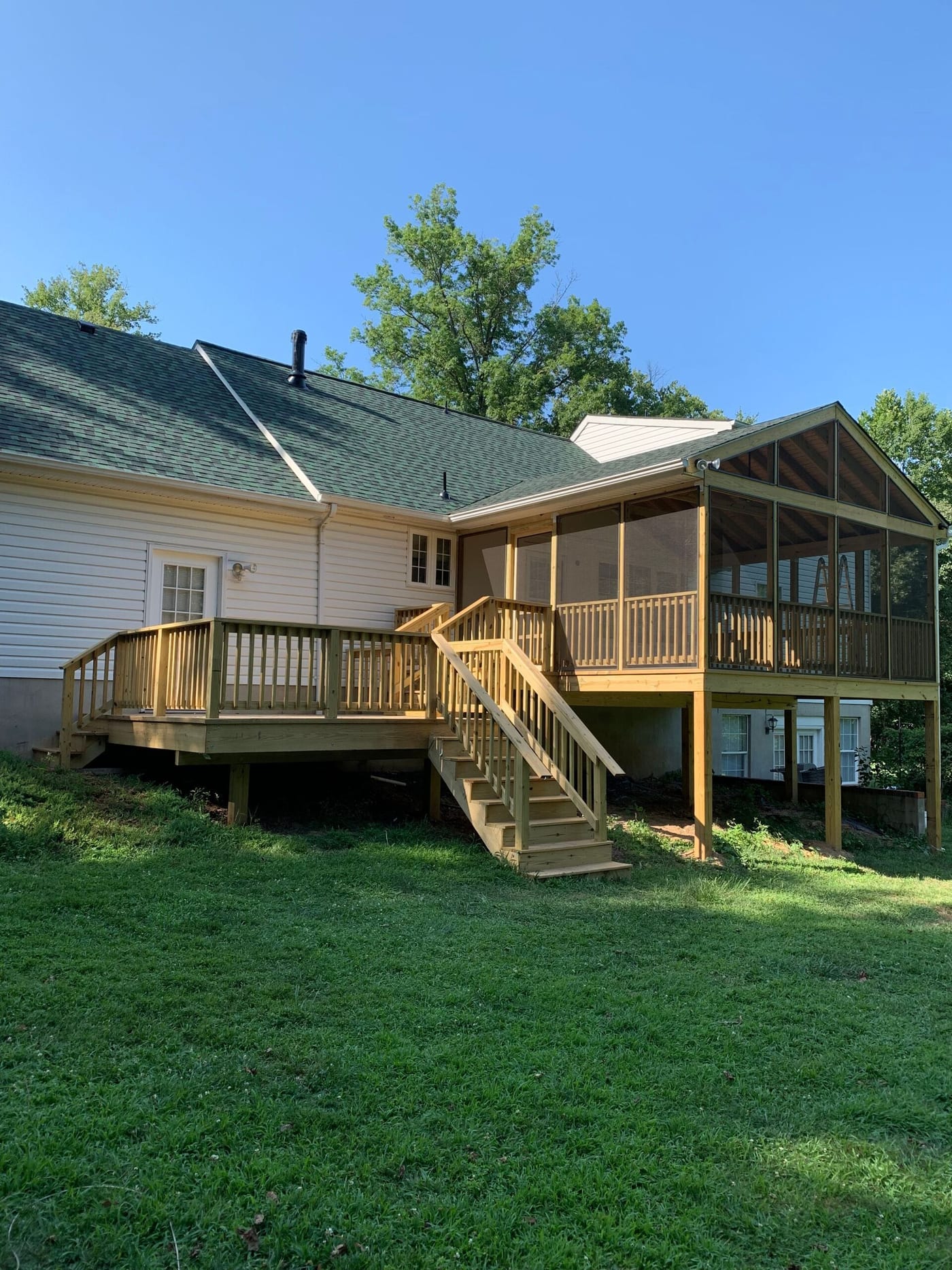 New wooden deck and screened porch on the back of a white single-storey home
