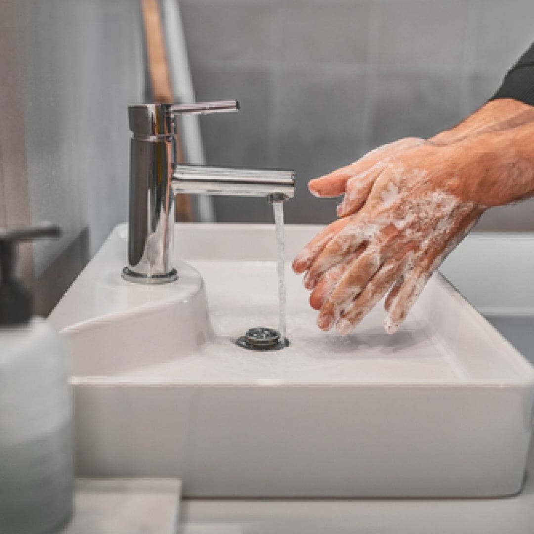 Hands being lathered under a chrome tap over a white basin